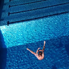 Ein junger Mann der breitbeinig in ein Schwimmbecken springt.