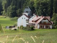 Zu sehen ist ein weißes Haus mit Balkon und Fensterläden. Dahinter befindet sich ein weiteres Haus und ein Silo.